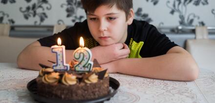 Teen boy looks thoughtfully at cake with candles on twelfth day of birth