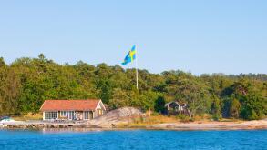 Sweden, Stockholm - House on island in archipelago with swedish flag on pole.