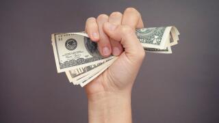 Woman hand squeezes dollar bills against grey background.