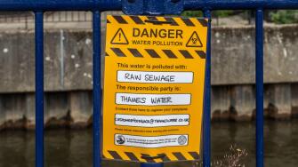 Protest sign reading Danger water pollution, this water is polluted with raw sewage. The responsible party is Thames Water. River Wey, Guildford, UK