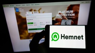 Person holding smartphone with logo of Swedish property platform company Hemnet AB on screen in front of website. Focus on phone display.