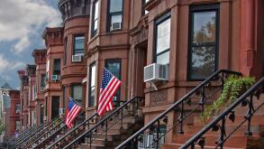 Brownstone row houses in Brooklyn neighborhood with US flags and cloudy sky