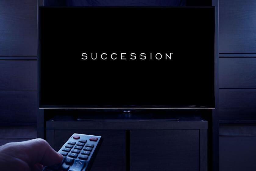 A man points a TV remote at the television which displays the Succession main title screen