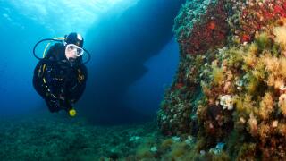 Female scuba diver fitted with Aqua Lung diving equipment near an underwater arch in Ses Salines Natural Park (Formentera, Mediterranean sea, Spain)