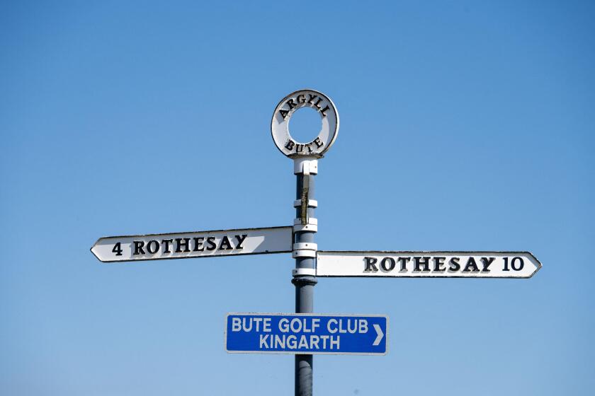 An island road sign on the Isle of Bute, Scotland against a blue sky. It shows the same destination, Rothesay, in two directions.