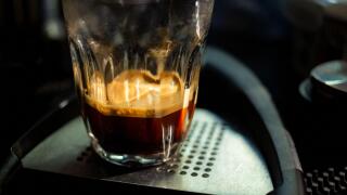 Close focus on double shot of hot espresso coffee on glass cup with dark scene of table.