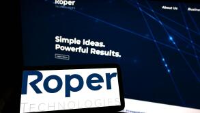Person holding smartphone with logo of US engineering company Roper Technologies Inc. on screen in front of website. Focus on phone display.