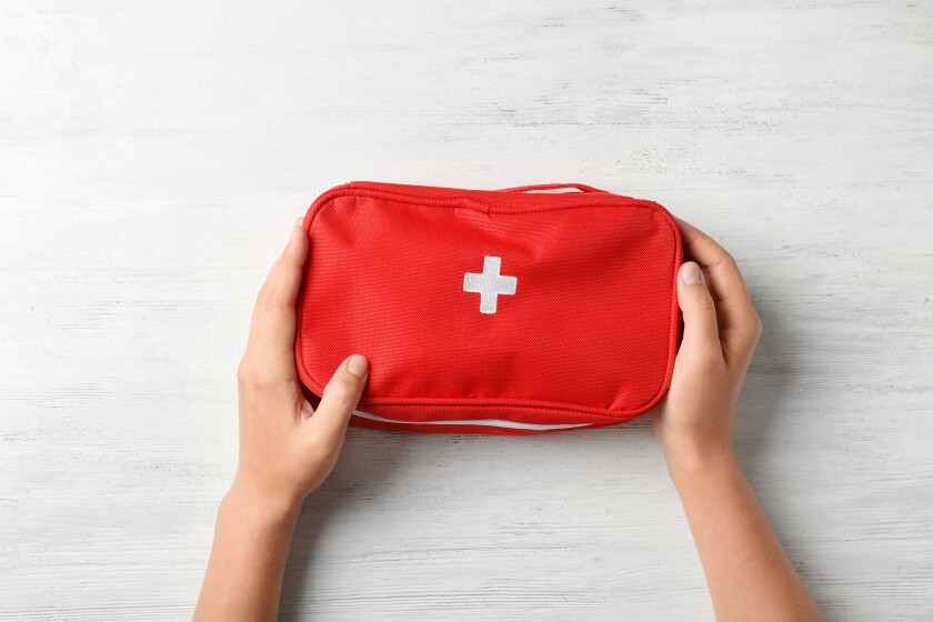 Woman holding first aid kit on wooden background, top view