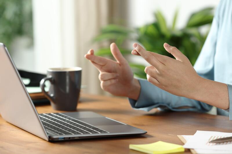Close up of an office worker hands crossing fingers checking laptop on wooden table at office