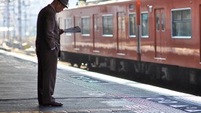 An elderly man reading a newspaper while waiting for a train.
