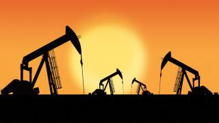 Rows of oil pumpjacks silhouette against a sunset sky with copy space. Oil and gas energy exploration.