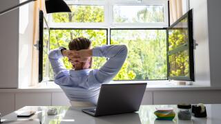 Relaxed Young Businessman Relaxing On Chair Behind Desk At Office