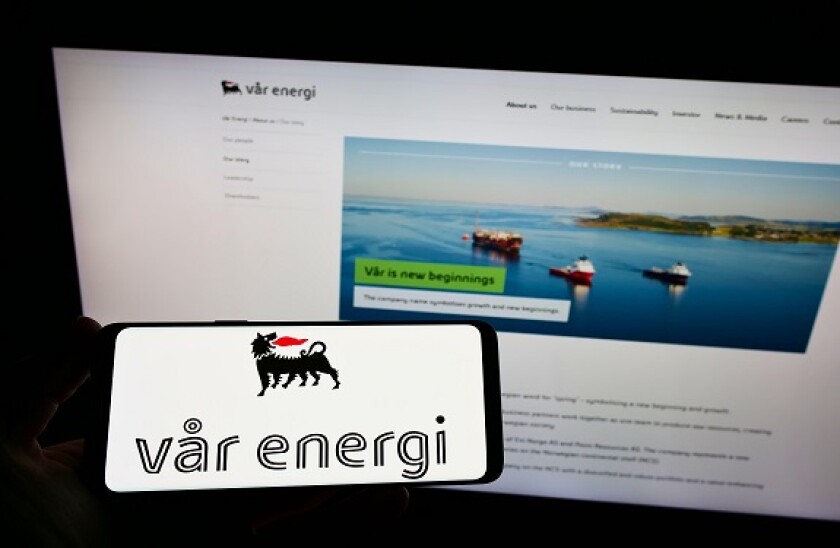 Person holding smartphone with logo of Norwegian oil and gas company Var Energi on screen in front of website. Focus on phone display.