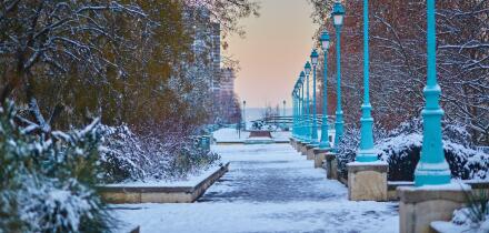 Winter cityscape of Paris with a snowy walkway lined with street lamps and trees, captured at sunrise