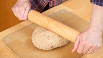 Woman rolling ball of bread dough with a rolling pin to flatten it, prior to forming it into a loaf. (MR)