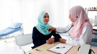 A young beautiful Muslim doctor is using a stethoscope to listen to the patient's heartbeat and write a report at the table in the hospital examinatio
