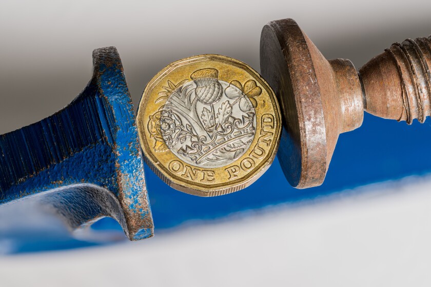 UK one pound sterling coin being squeezed between the solid jaws of a vise or vice