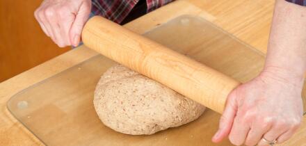 Woman rolling ball of bread dough with a rolling pin to flatten it, prior to forming it into a loaf. (MR)