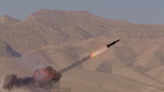 Fighting in a desert area. A missile soars into the sky, leaving a trail of smoke behind it. Concept: military conflict in the Middle East