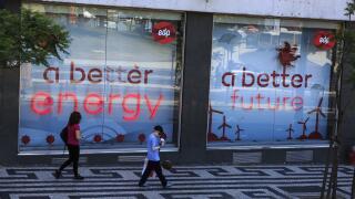 Two people walking past signs in the store window of EDP power company depicting a better energy a better future, Lisbon Portugal