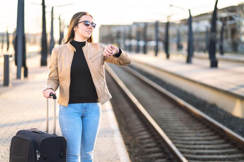 Woman looking at the time and watch while waiting for train. Smiling and happy female traveler standing at station and platform.