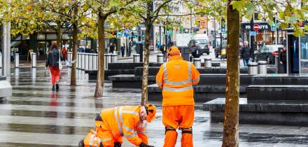 Two male employees of SGS in orange high-visibility clothing, making an inspection on the forecourt of King's Cross Station, London, UK