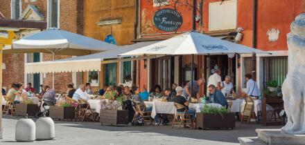 Restaurant piazza Italy, view in summer of a group of people dining outside a pizzeria in the scenic port of Chioggia, Comune of Venice, Italy