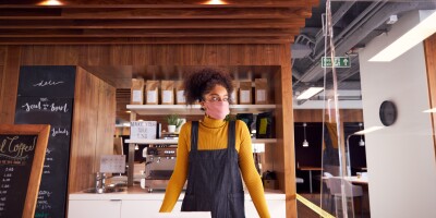 Female Small Business Owner Of Coffee Shop In Mask Standing Behind Counter During Health Pandemic
