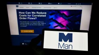 Person holding smartphone with logo of British financial company Man Group plc on screen in front of website. Focus on phone display.