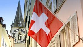 Clock tower of the St. Peter Church and Swiss Flag on the facade building in Zurich, Switzerland