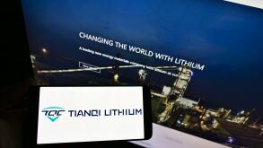 Person holding smartphone with logo of Chinese manufacturing company Tianqi Lithium Corp on display in front of web page. Focus on phone screen.