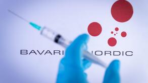 In this photo illustration a hand in medical gloves holds a syringe in front of Bavarian Nordic in Barcelona, Spain on September 2, 2021. Bavarian Nor