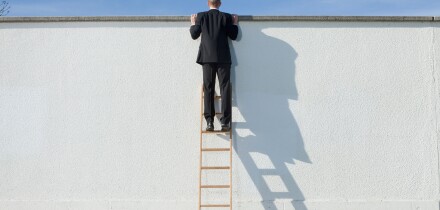 Businessman on ladder looking over wall