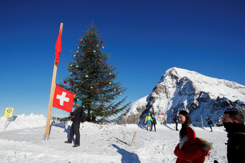 Tourists pose with a Swiss flag next to a Christmas tree and with the Eiger North Face at the Jungfraujoch in Lauterbrunnen, Switzerland December 7, 2017. REUTERS/Denis Balibouse