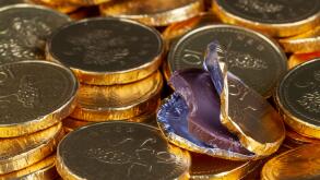 Chocolate money pile of gold coins. Edible sweets covered in foil as pretend money. One open coin half eaten