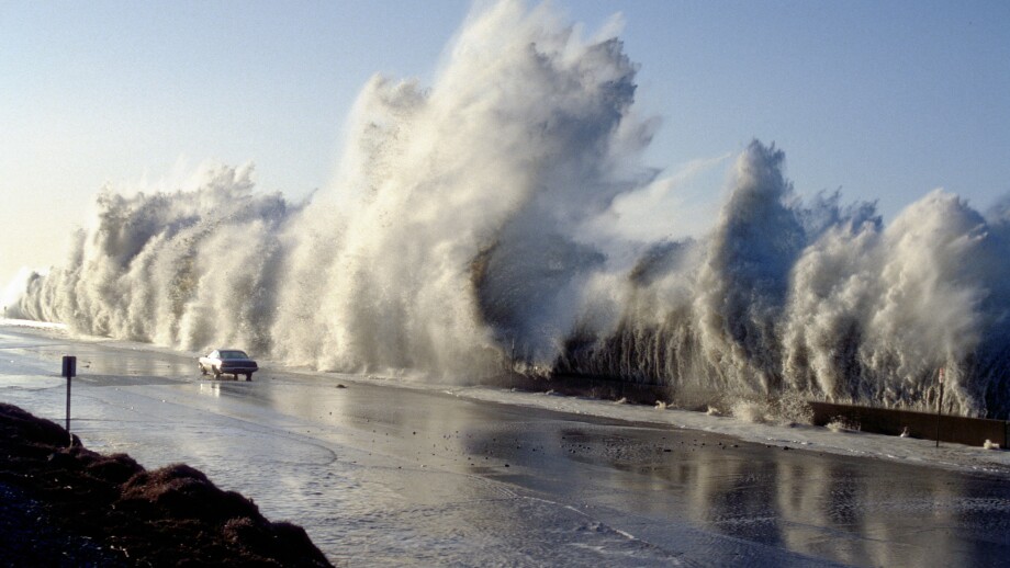 A huge storm surge wave dwarfs a car travelling on Highway 1 at Solimar Beach California