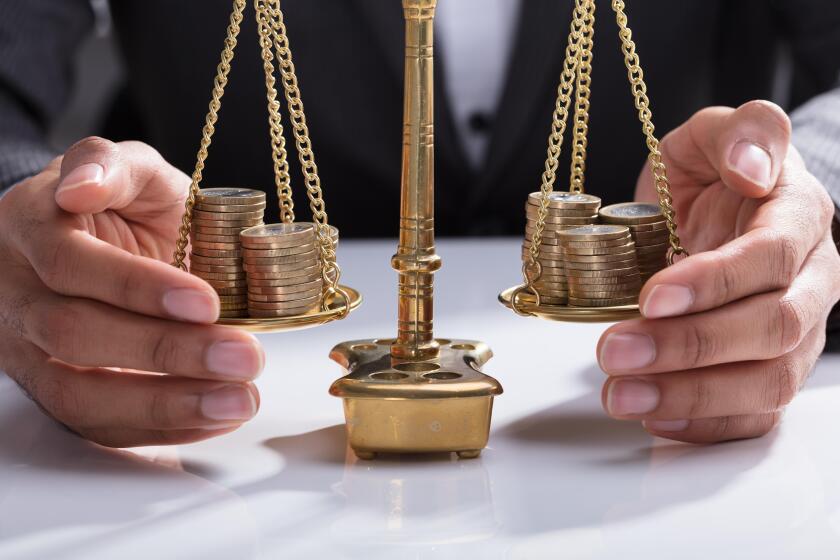 Close-up Of A Businessperson's Hand Covering Stacked Coins On Golden Weighing Scale