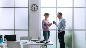 Cheerful office workers in the office, relaxing, having a coffee break and chatting together, they are standing in front of the