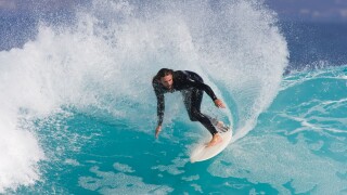 Surfer rides along azure blue wave.