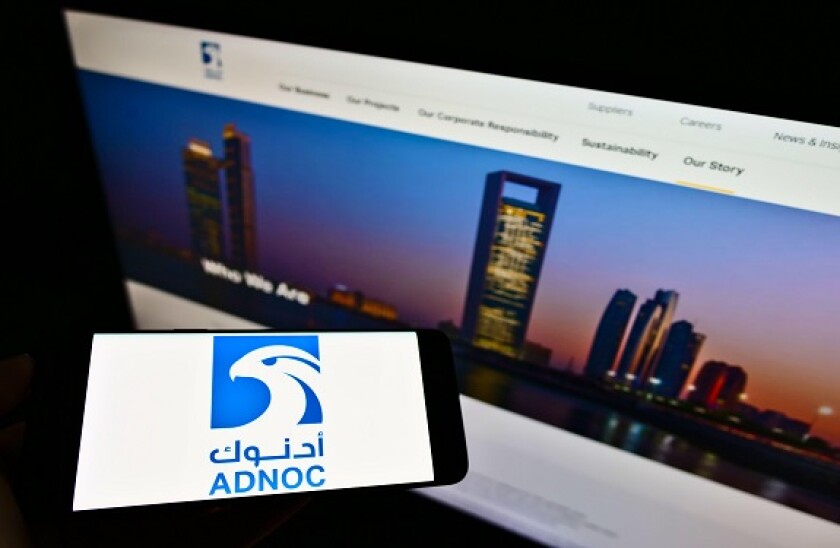 Person holding smartphone with logo of Abu Dhabi National Oil Company (ADNOC) on screen in front of website. Focus on phone display. Unmodified photo.