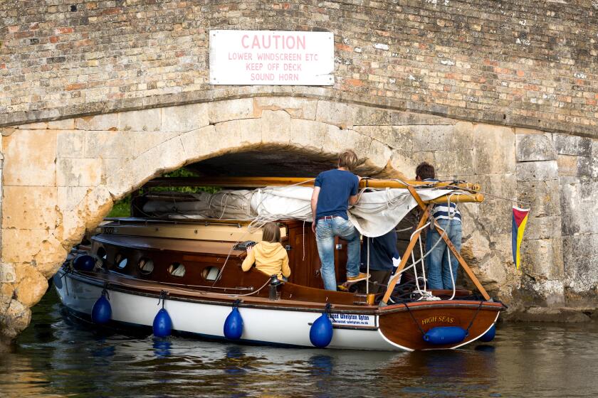 Small yacht carefully navigating the low bridge at Potter Heigham, on the Norfolk Broads, England UK