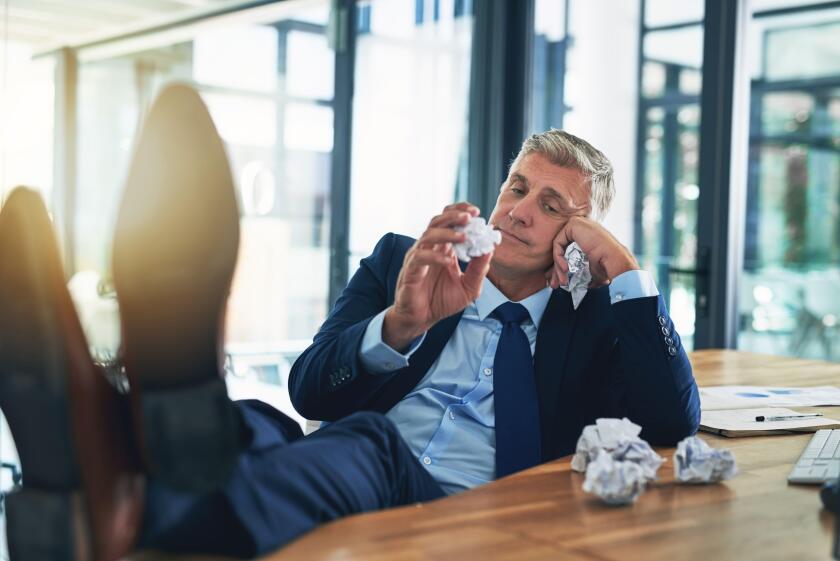 Just another humdrum day. a bored businessman crumpling pieces of paper at his desk.