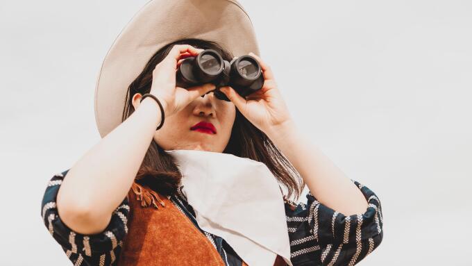 cute chinese cowgirl while looking at the horizon with binoculars on a wild west farm