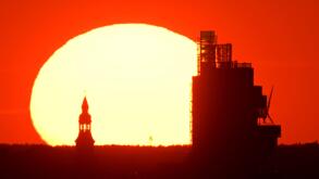 Hanover, Germany. 10th Aug, 2022. The sun sets behind the Norddeutsche Landesbank NordLB. The photo was taken with extreme telephoto focal length from just under eight kilometers away from the Kronsberg on the outskirts of Hanover. Credit: Julian Stratens