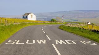 White slow painted sign on B6277 road, barn in flower meadow. Forest in Teesdale, North Pennines, Durham Dales, County Durham.