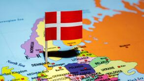 A map of Denmark with the national flag of Denmark on it. The flag is red with a white Nordic cross. Travel and government concept