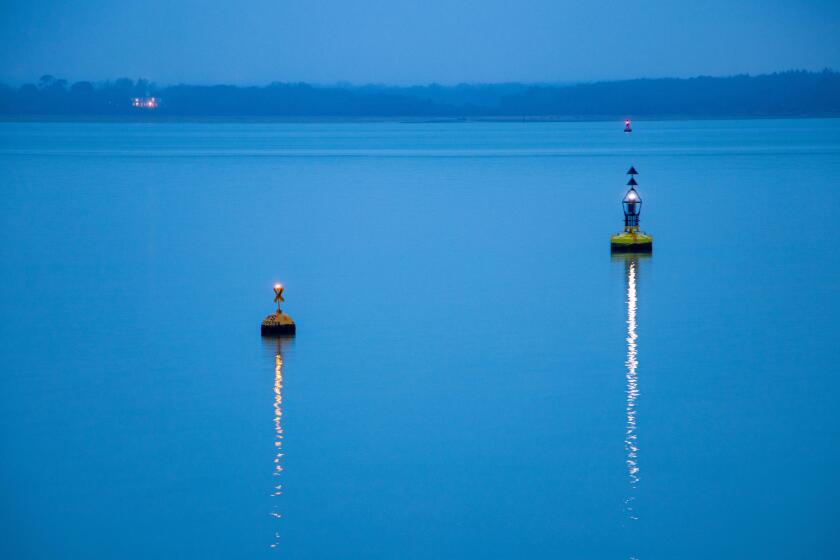 Two buoys marking the navigation channel.  Lights reflected on the water on a calm evening in winter.  The sea is pale blue.