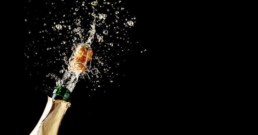 Champagne cork popping and splashing on black background