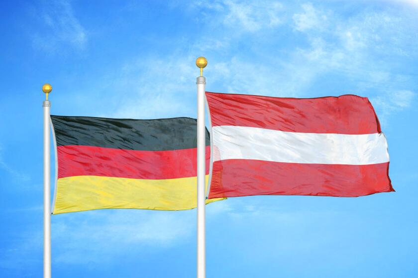 Germany and Austria two flags on flagpoles and blue cloudy sky