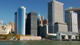 Modern skyscrapers line the waterfront in Lower Manhattan?s Financial District, New York City, with clear blue skies and calm water below